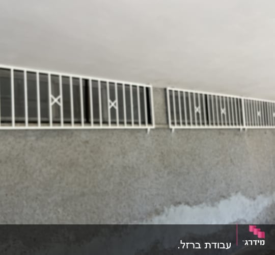 סורגים לבנים על חלונות קטנים בקיר בטון אפור